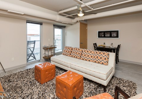 A living room with a white couch and orange ottoman.