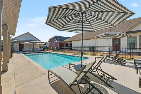 A striped umbrella is over a lounge chair by a pool.