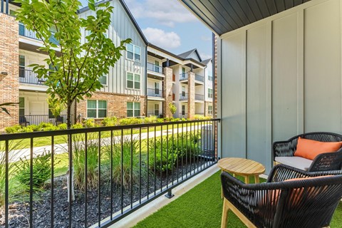 A balcony with a chair and a table overlooking a grassy area.
