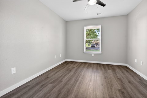 A room with a ceiling fan and a window showing a view of a street.