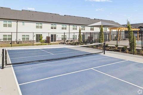A tennis court is surrounded by a fence and a building.