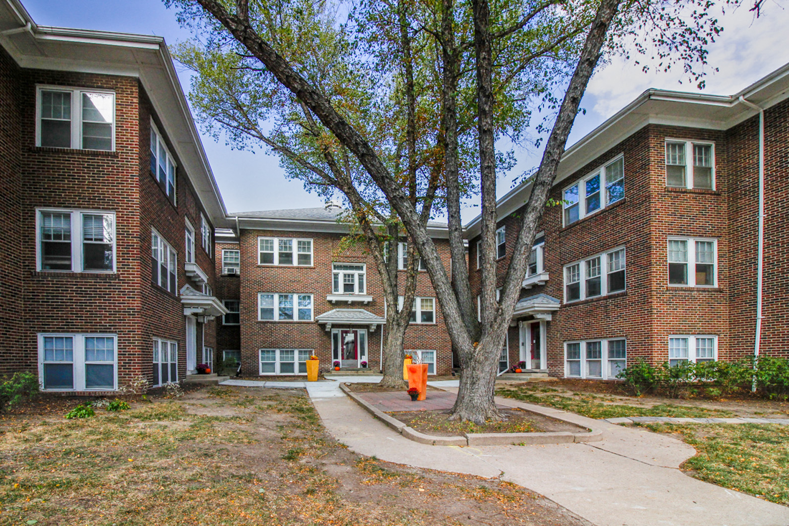 an apartment building with a sidewalk and a tree in front of it