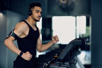 A man in a black tank top is running on a treadmill.