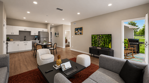 A modern living room with a grey couch, a black coffee table, and a kitchen area in the background.