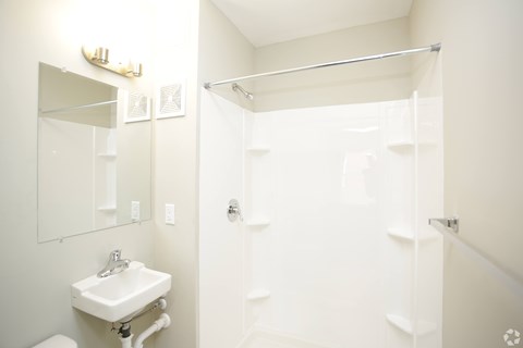 A white bathroom with a sink, mirror, and shower.