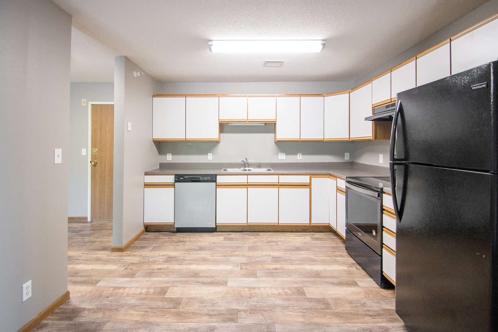 an empty kitchen with white cabinets and a black refrigerator