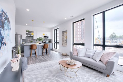 A modern living room with a grey sofa and a kitchen area in the background.