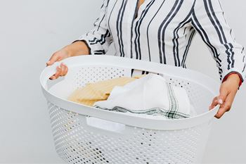 A person holding a white laundry basket with clothes inside.