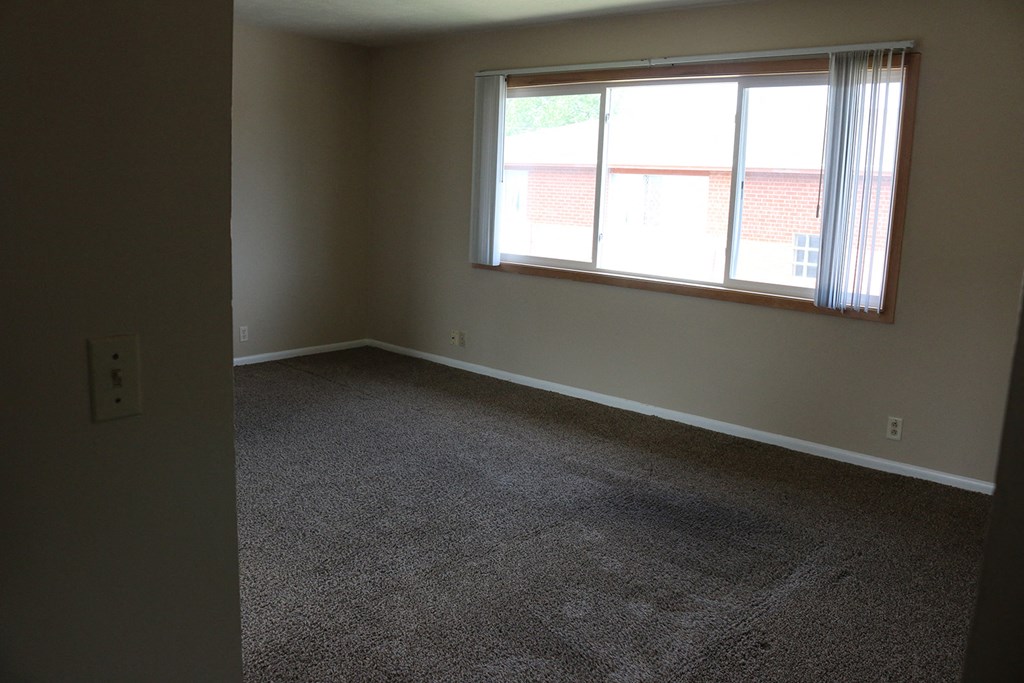 an empty living room with a window and carpet