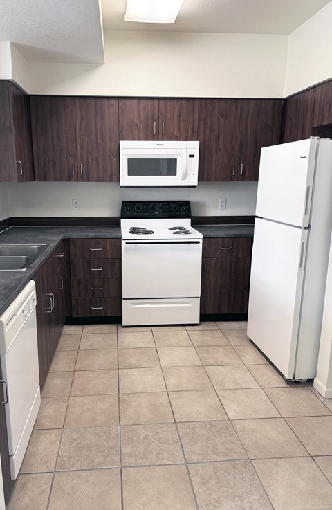 A kitchen with a white refrigerator, black countertops, and brown cabinets.