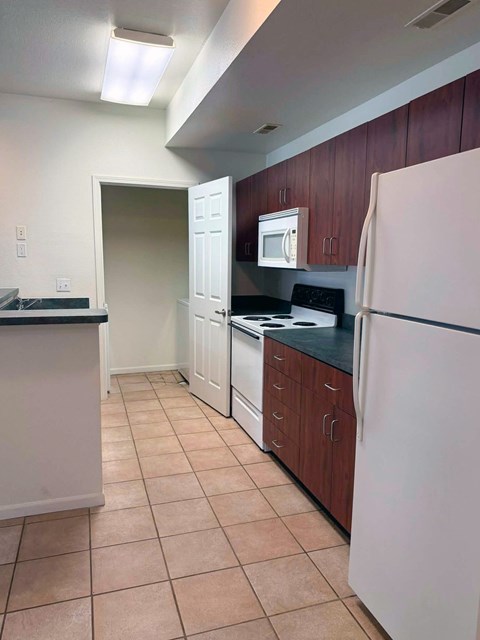 A kitchen with a white refrigerator, black countertops, and brown cabinets.