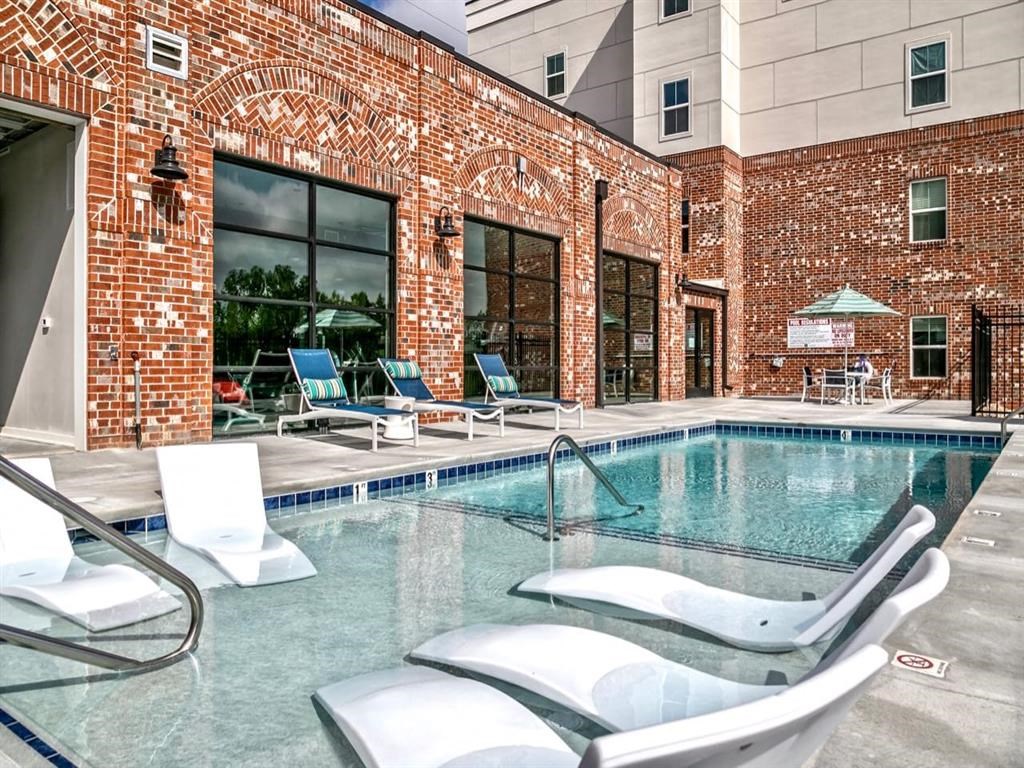 a swimming pool with four lounge chairs in front of a brick building