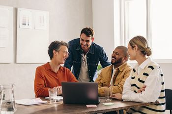 a group of people sitting around a table with a laptop
