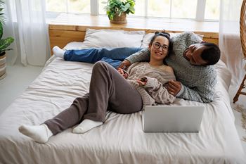 A man and woman are lying on a bed with a laptop.