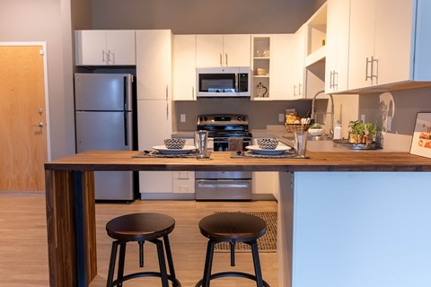 A kitchen with a refrigerator, microwave, and a counter with two stools.
