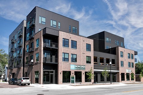 A modern multi-story building with a black and brown exterior and a "Now Open" sign on the ground floor.