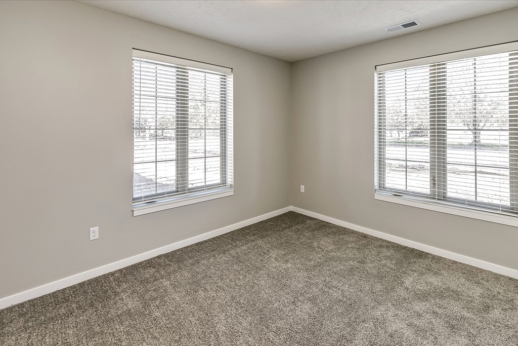 an empty bedroom with two windows and carpeting