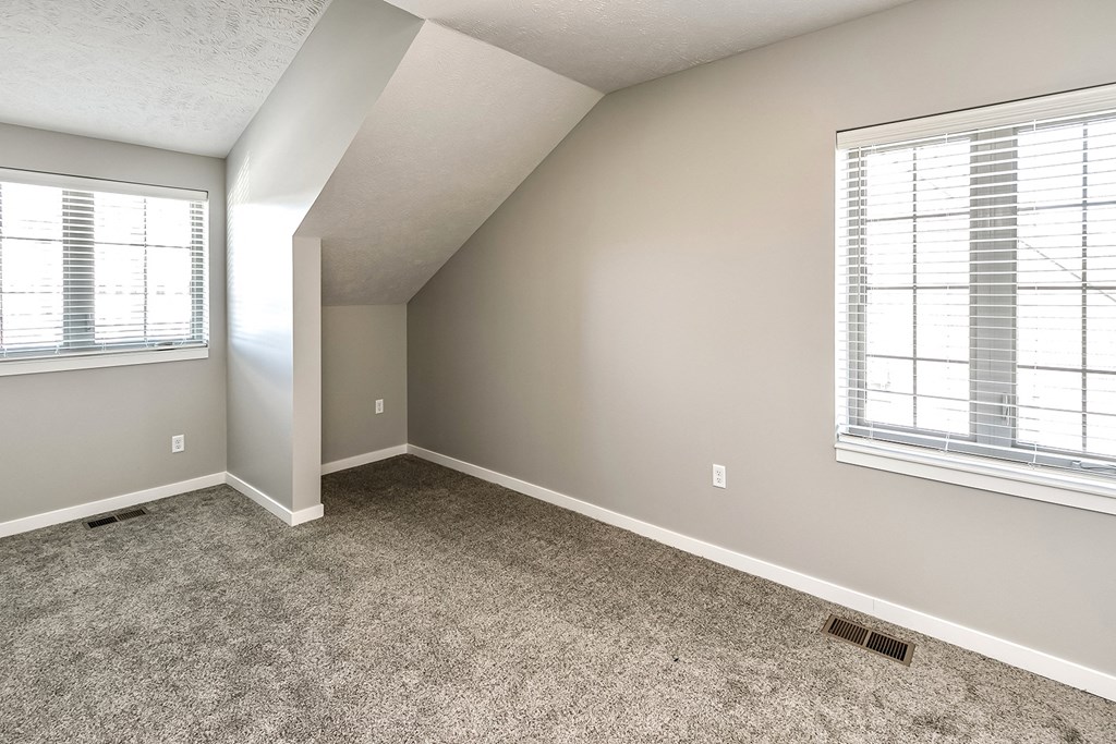 an empty bedroom with carpet and two windows