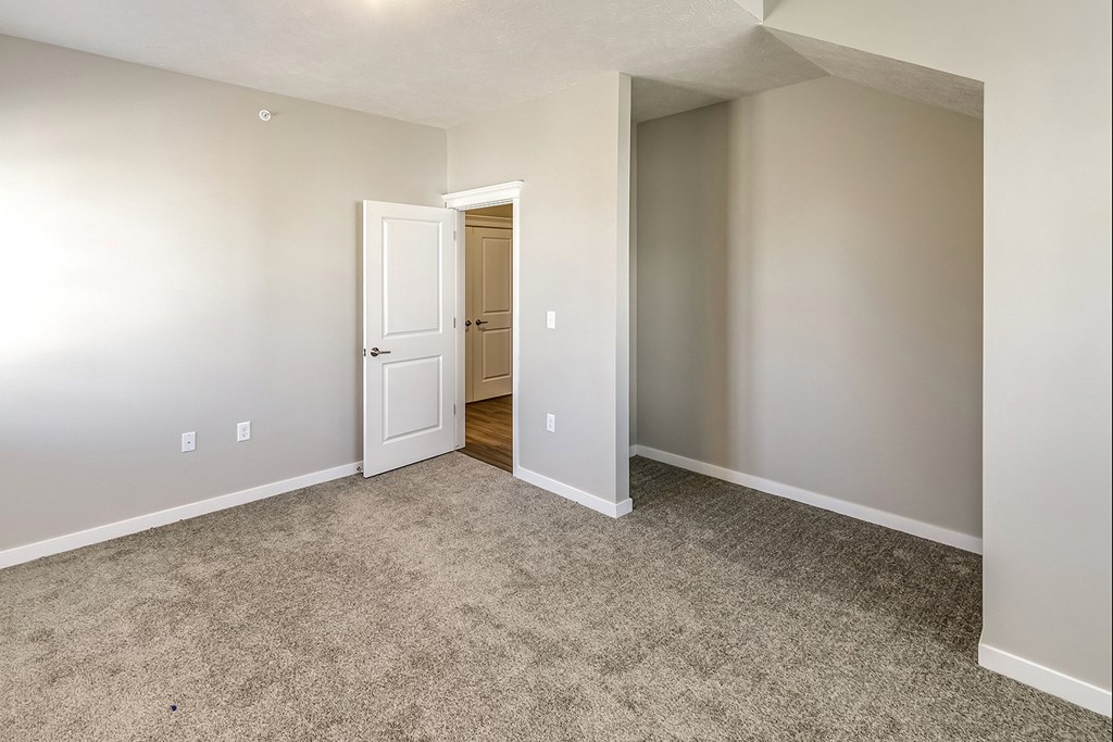 an empty living room with carpet and a door to a bathroom