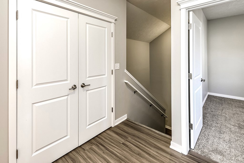 an empty entryway with white doors and a stairwell in a home