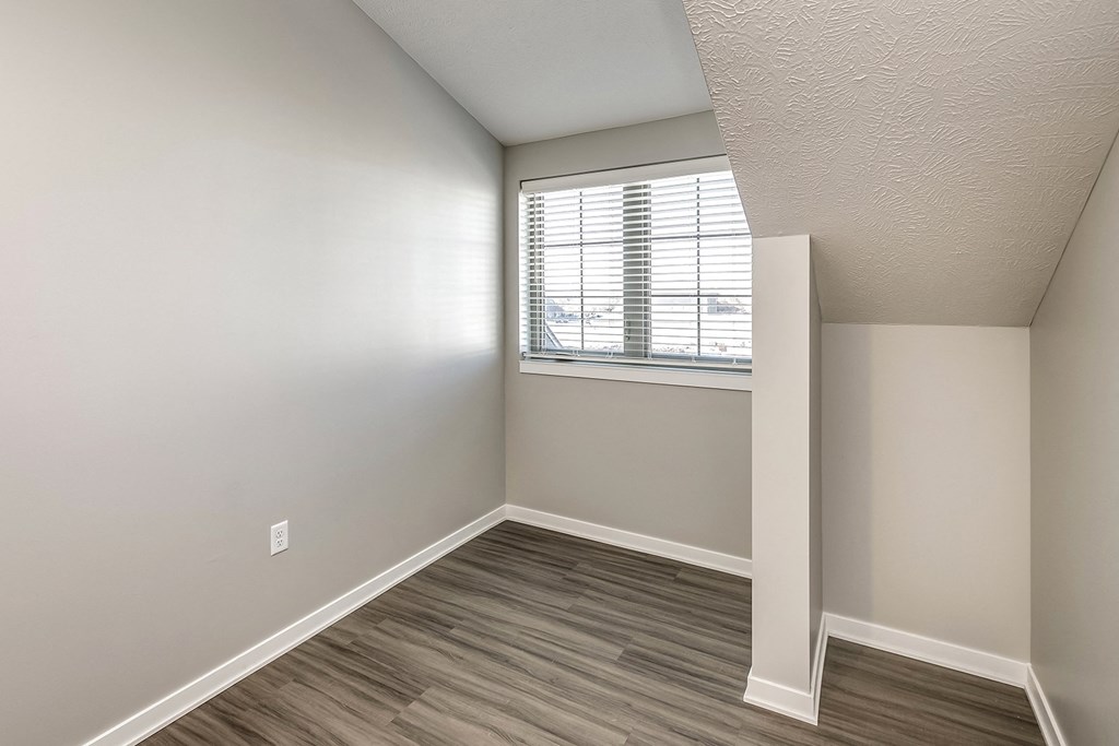 an empty bedroom with a window and wood flooring