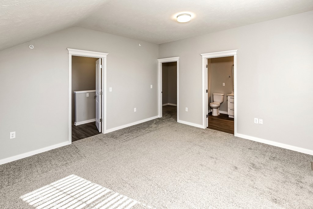 an empty living room with two doors to the bathroom and a rug
