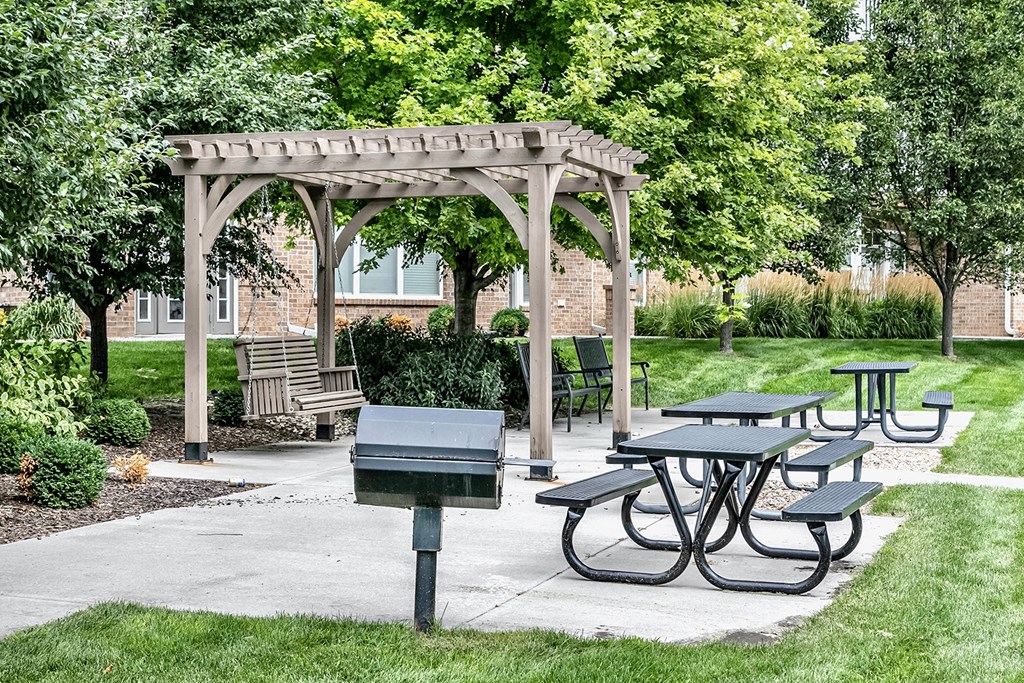 a picnic area with picnic tables and a grill at Legacy Commons Apartments in Omaha, NE