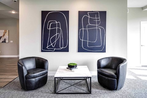 two chairs and a table in a living room with paintings on the wall