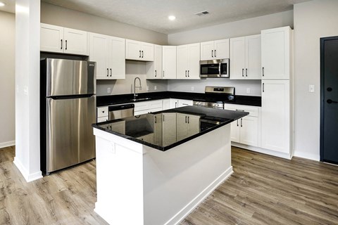 a white kitchen with black counter tops and stainless steel appliances
