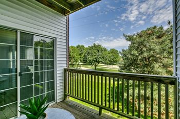 A balcony with a potted plant and a view of a green lawn.