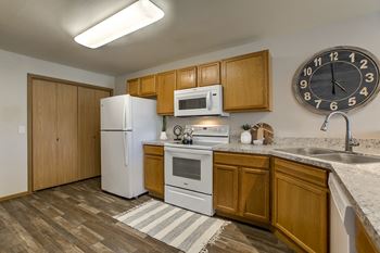 A kitchen with a white refrigerator, wooden cabinets, and a clock on the wall.