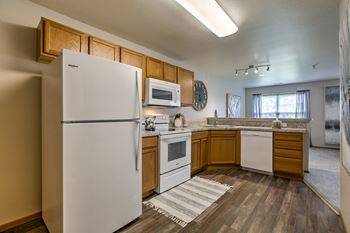 A white refrigerator stands in a kitchen with wooden cabinets and a striped rug on the floor.