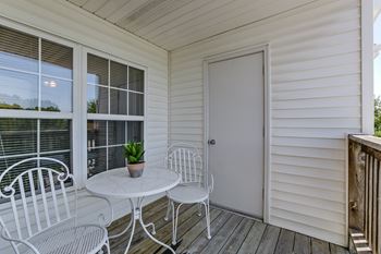 A small white table with two chairs is on a porch.