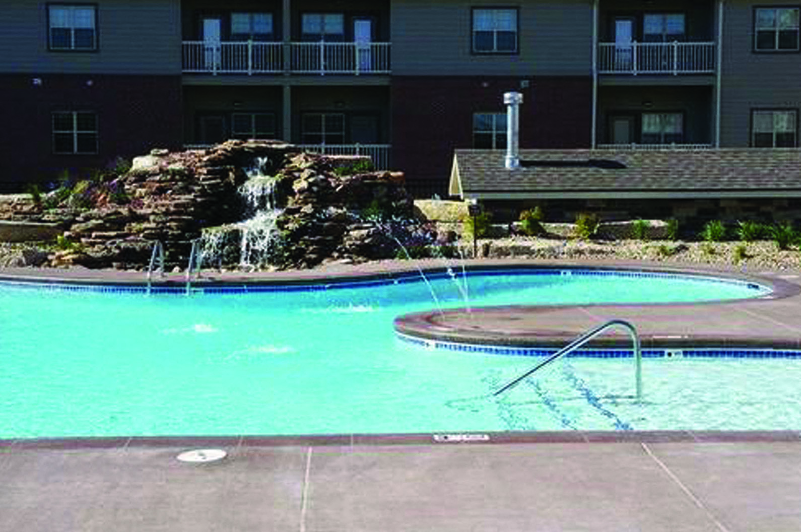 a swimming pool with a waterfall in front of an apartment building