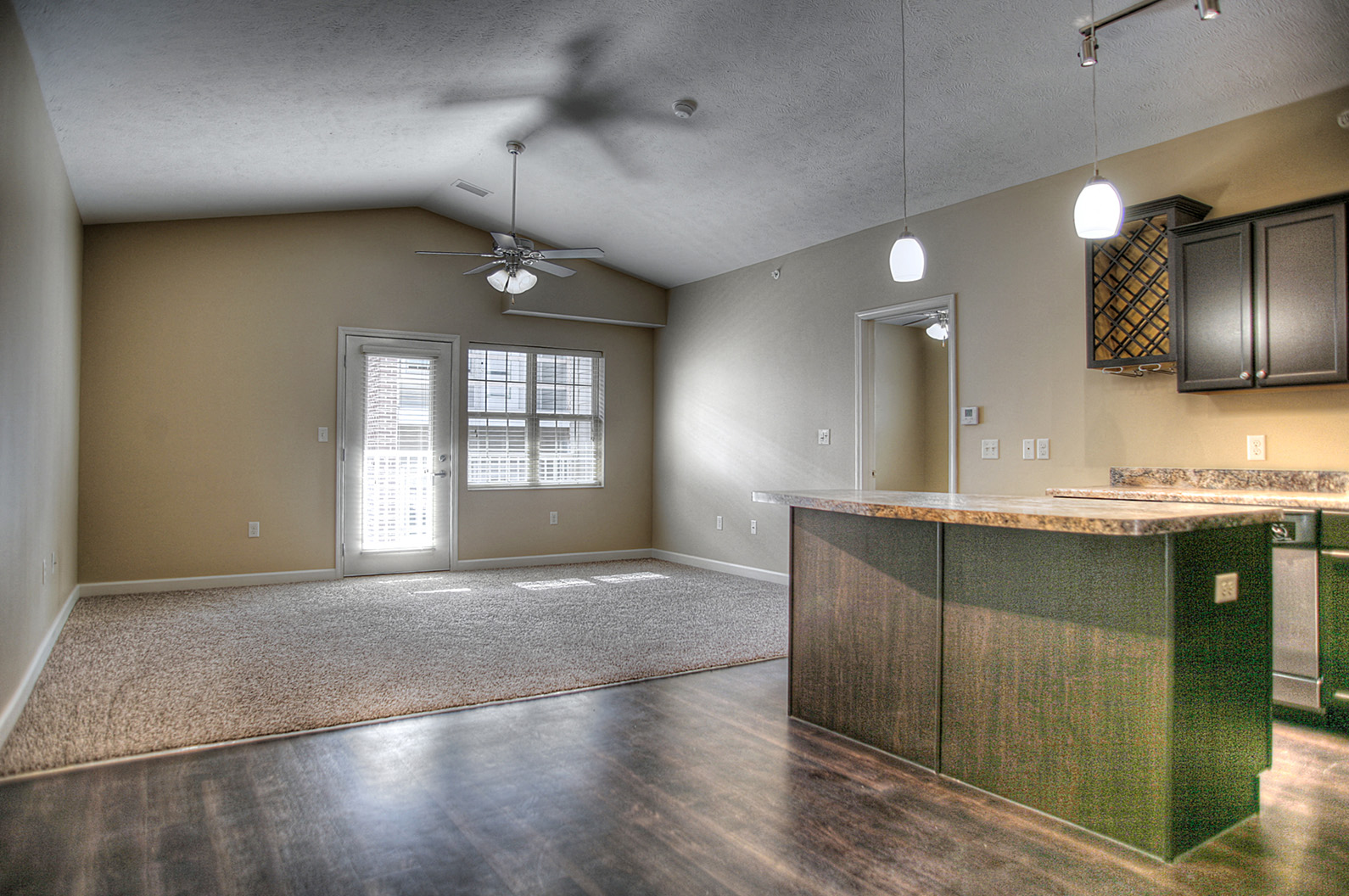 an empty living room with a kitchen and a ceiling fan