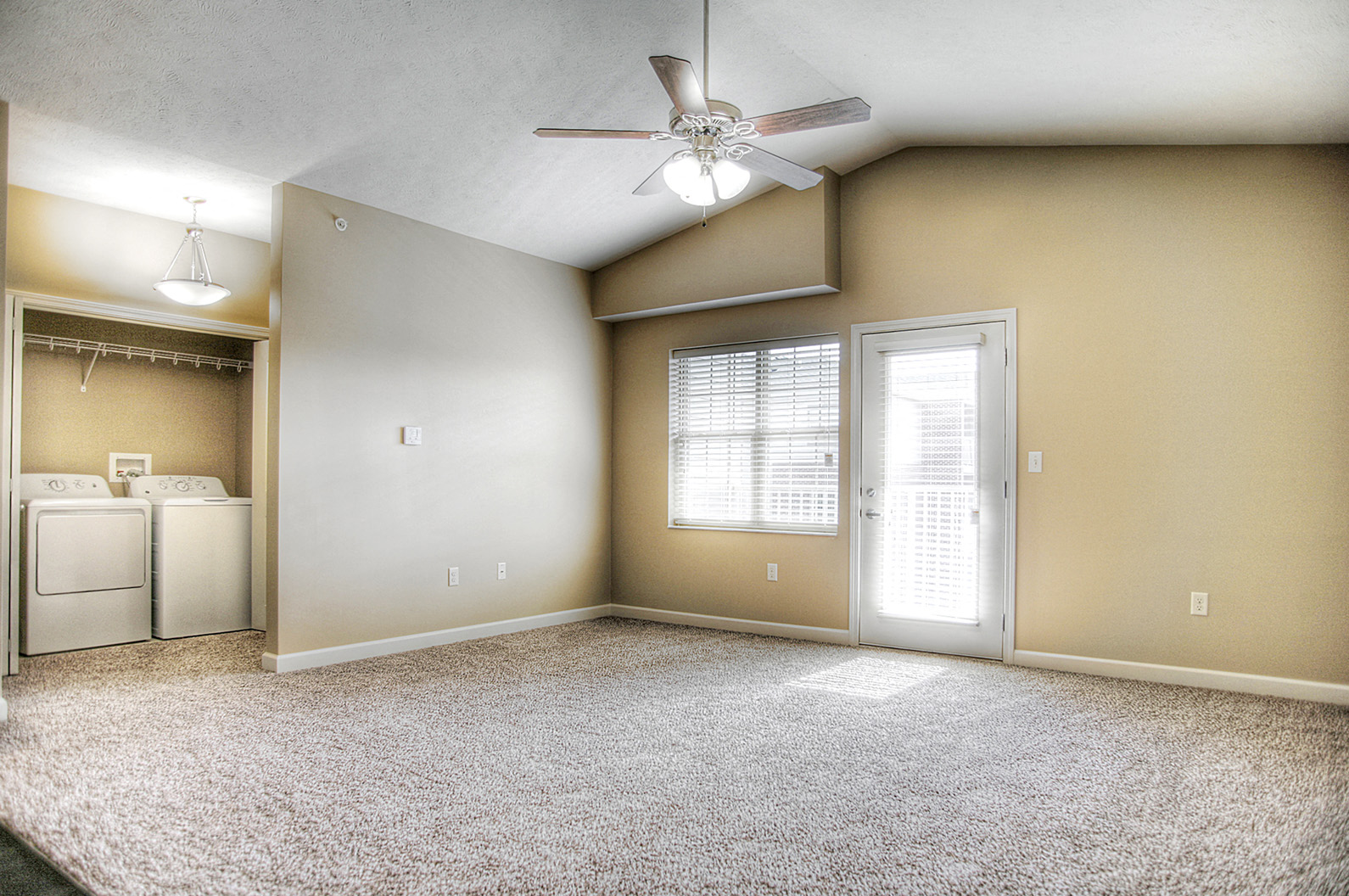 an empty living room with a ceiling fan and a door to a kitchen