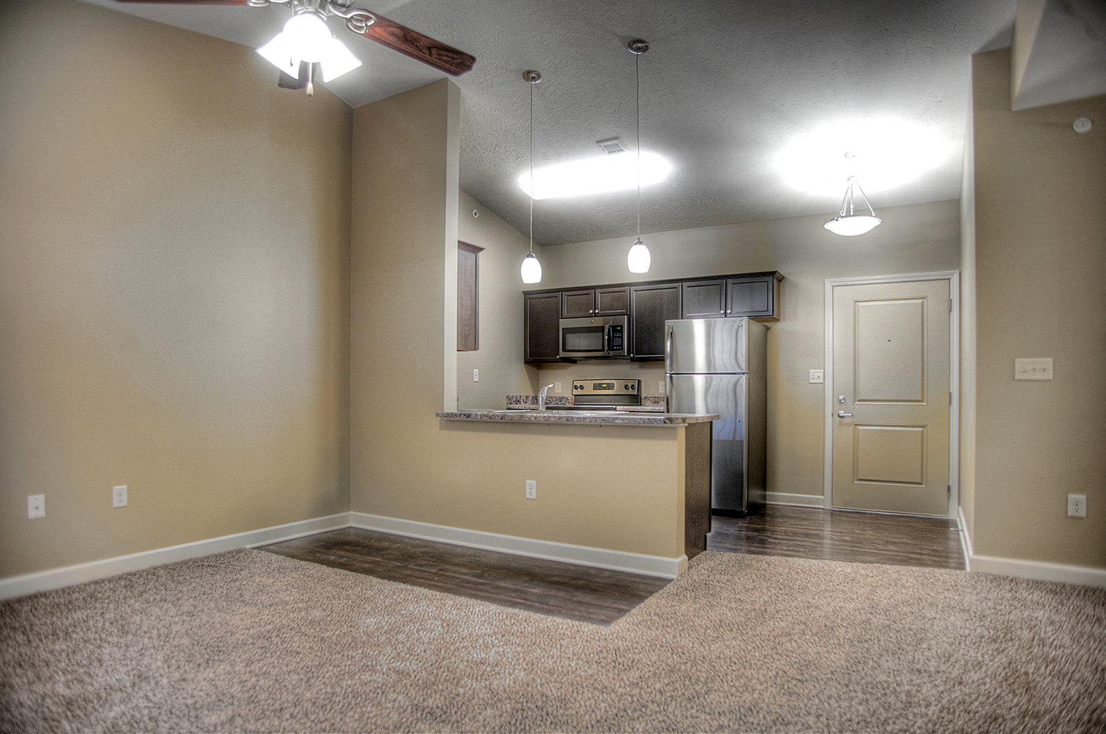 an empty living room with a kitchen in the background