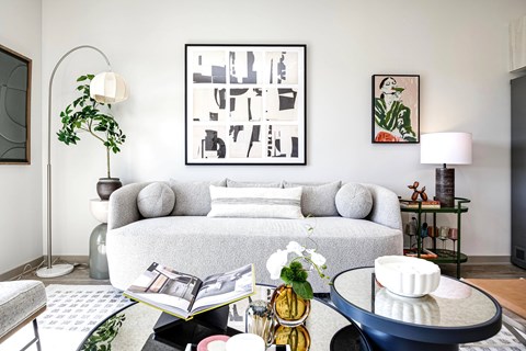 A living room with a grey couch, a coffee table, and a large abstract painting on the wall.