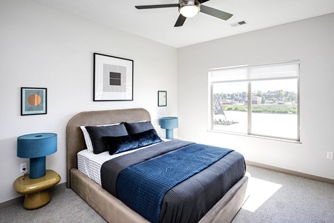 A bedroom with a bed, a ceiling fan, and a window overlooking a landscape.