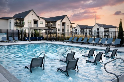 A pool with chairs and a building in the background.