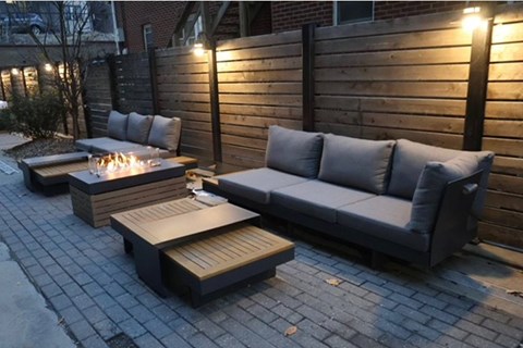 A grey couch and a table with a fire pit in front of a wooden fence.
