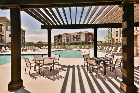A wooden pergola over a pool with chairs underneath.