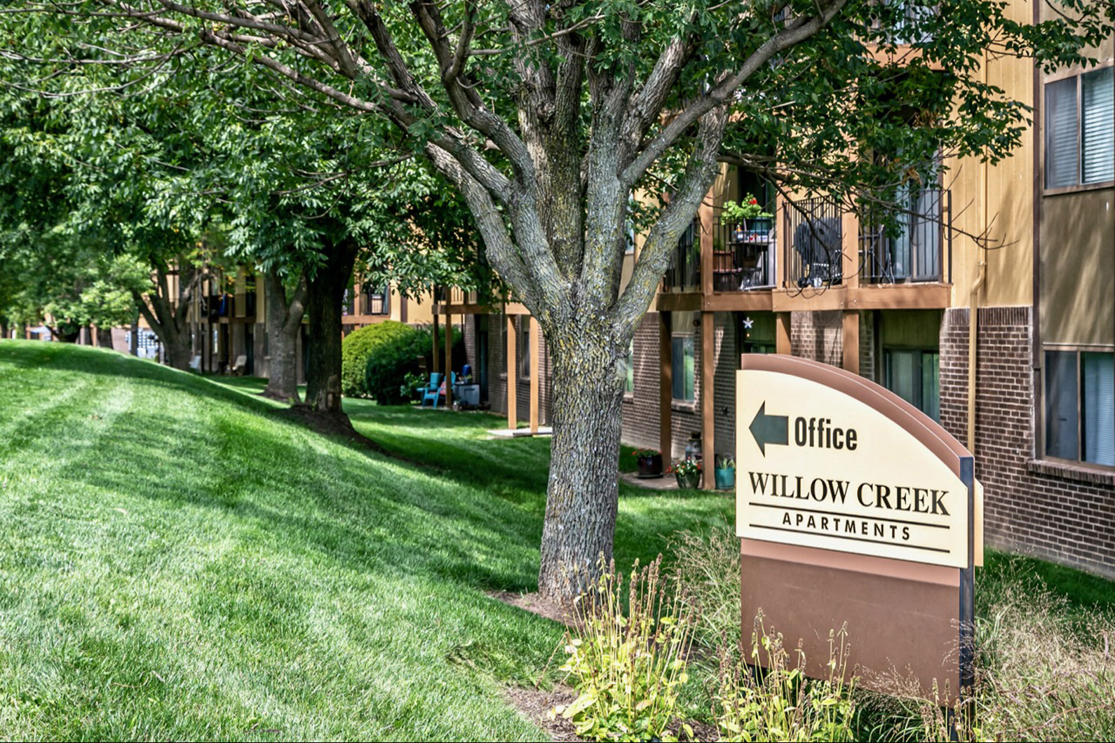 a sign for office willow creek apartments in front of a tree