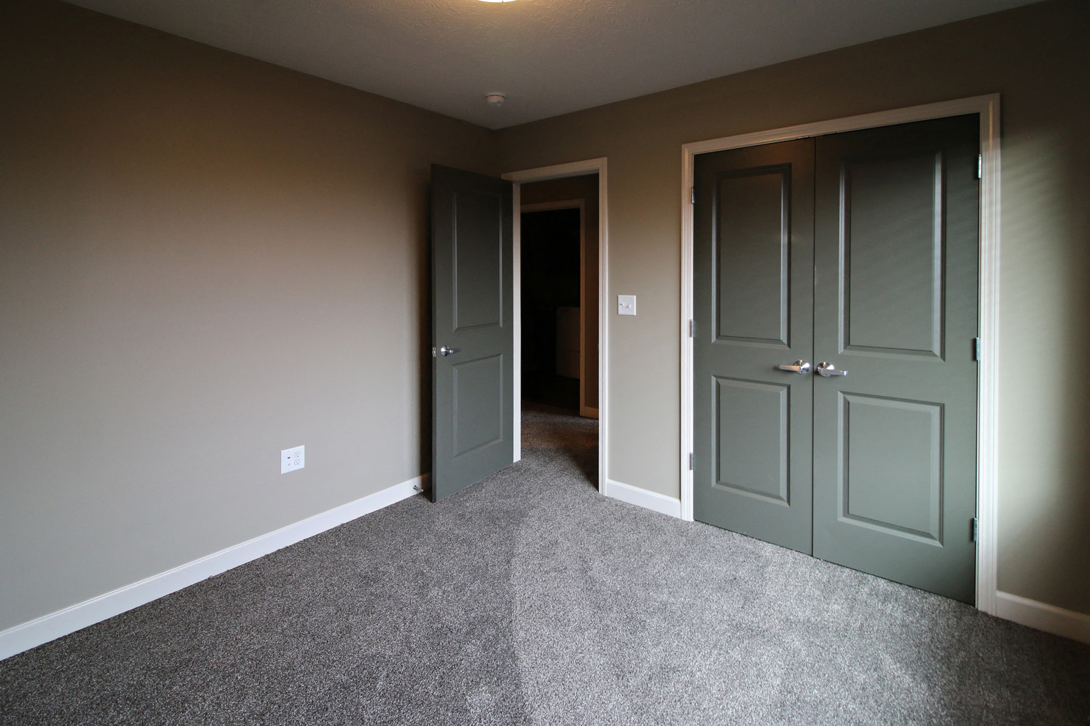 a carpeted room with two doors and a hallway to a closet