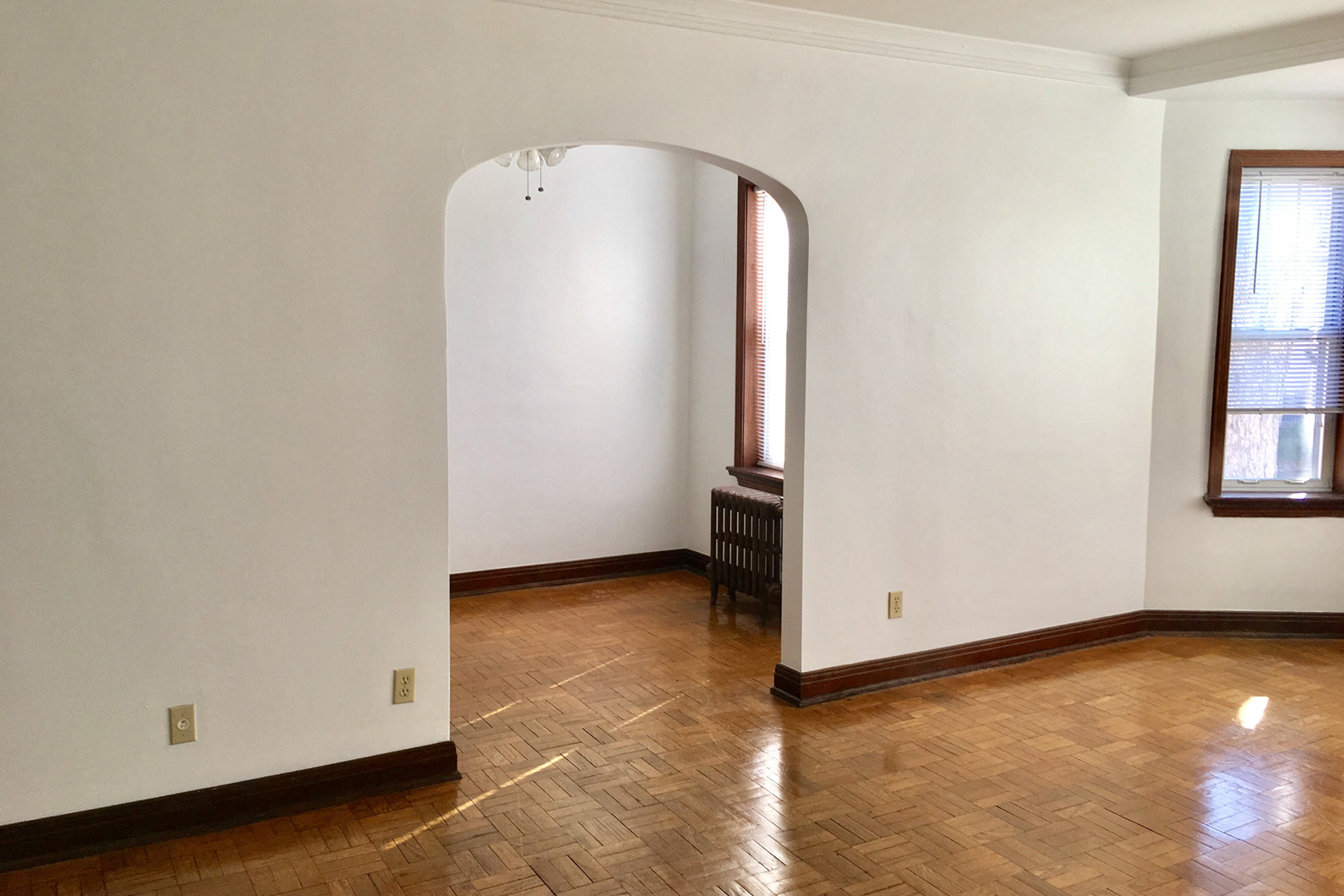 an empty living room with white walls and wooden floors and an arched doorway