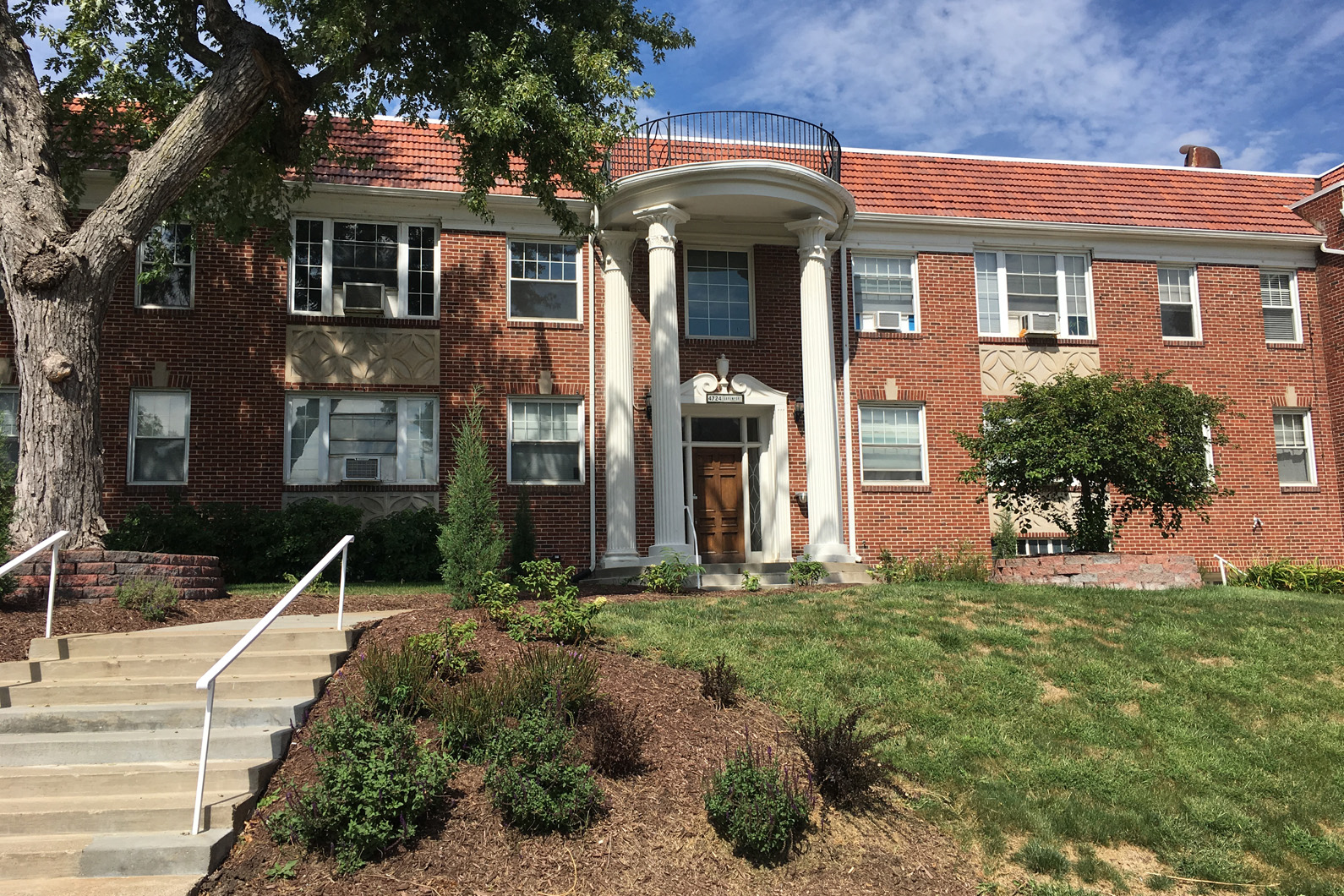 the front of a brick building with stairs and a tree