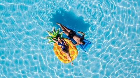 A person is floating on a pineapple in a pool.