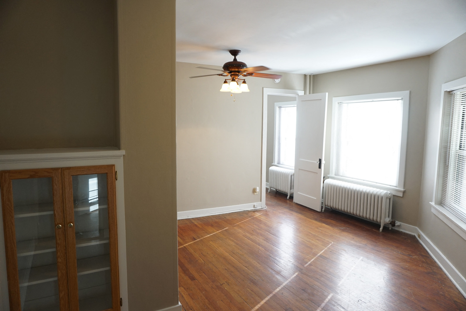 an empty living room with a ceiling fan and a cabinet