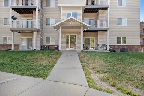 Apartment building with a front lawn and a walkway leading to the entrance.