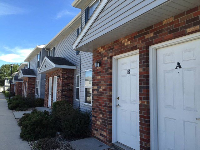 a brick house with two white doors and a sidewalk
